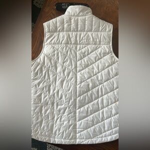 White UA Storm vest white w/ 3 zip pockets, one upper chest exterior pocket.